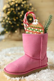 Photo of Saint Nicholas day tradition. Boot with sweets and artificial snow on floor indoors, closeup