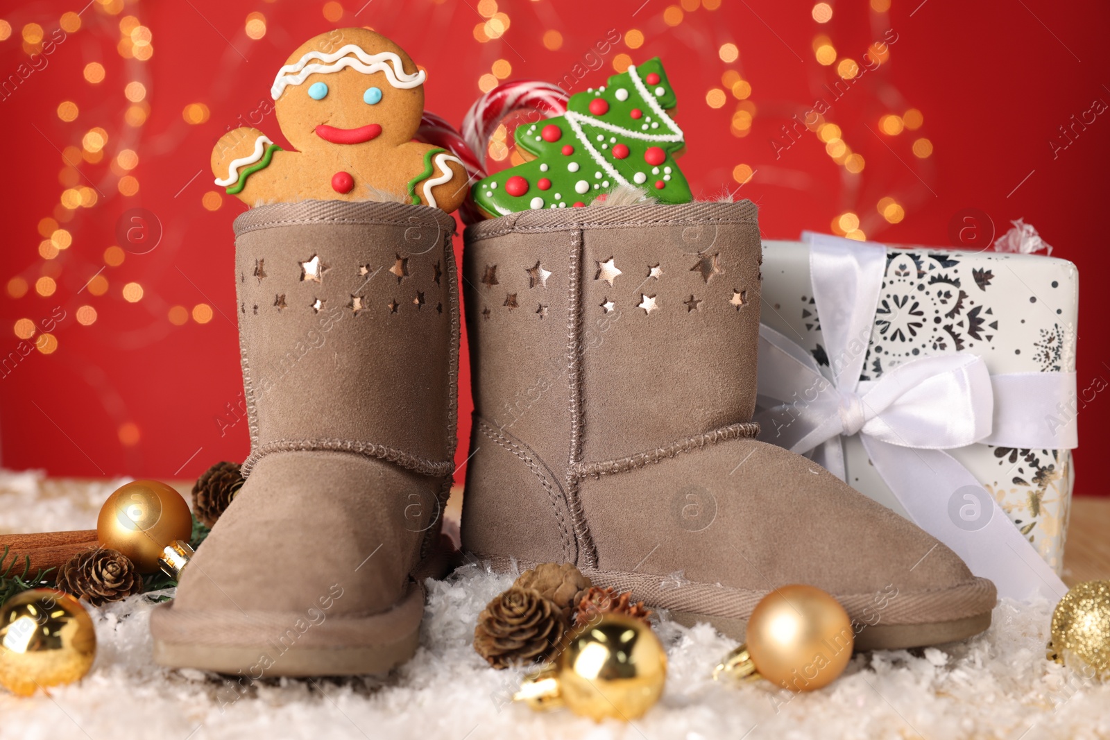Saint Nicholas day. Boots filled with treats, festive decor and gift box on table against red background with blurred lights. Bokeh effect Photo of Saint Nicholas day. Boots filled with treats, festive decor and gift box on table against red background with blurred lights. Bokeh effect