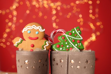 Photo of Saint Nicholas day. Boots filled with treats on red background with blurred lights, closeup. Bokeh effect