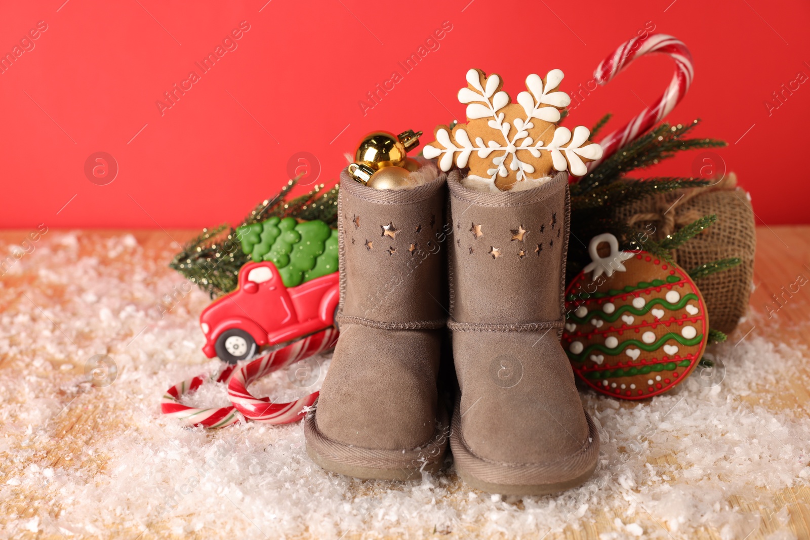Photo of Saint Nicholas day. Boots with treats and festive decor on table against red background, space for text