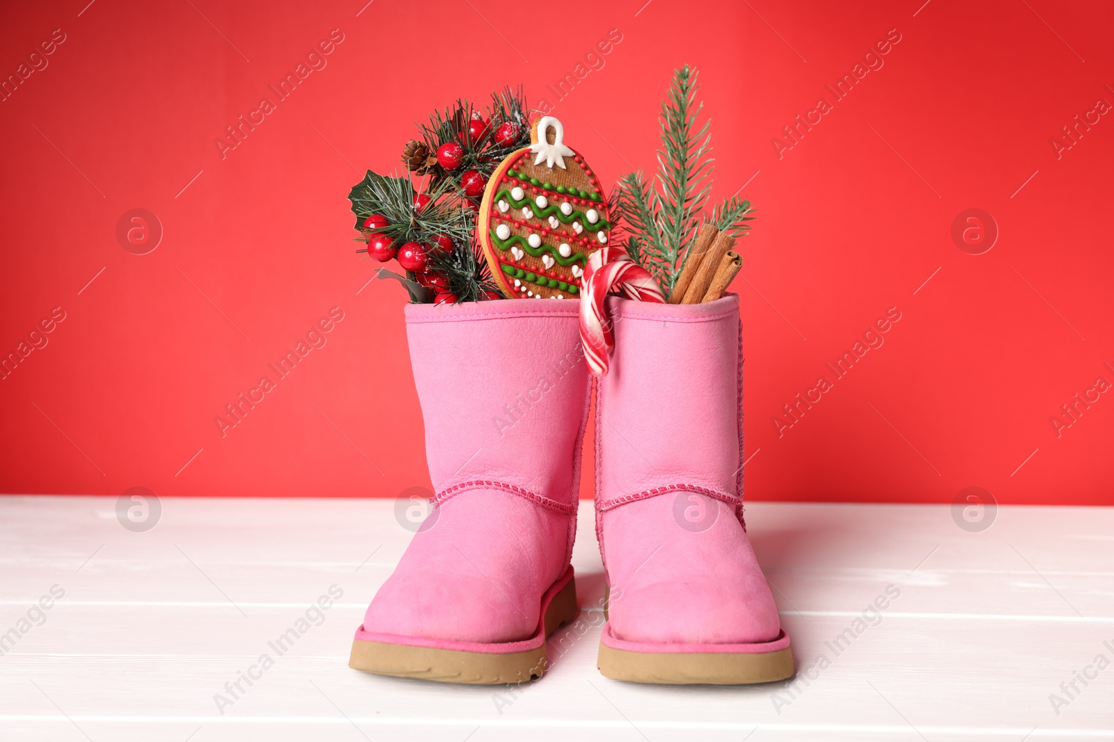 Photo of Saint Nicholas day. Boots with treats and festive decor on white wooden table against red background