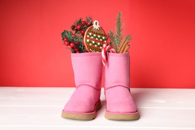 Photo of Saint Nicholas day. Boots with treats and festive decor on white wooden table against red background