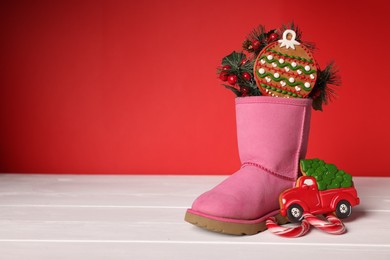 Photo of Saint Nicholas day. Boot with treats and festive decor on white wooden table against red background, space for text