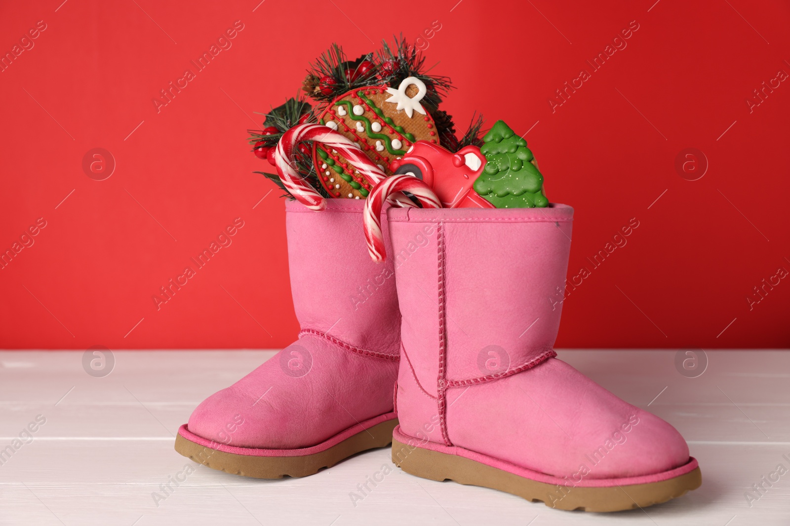 Photo of Saint Nicholas day. Boots with treats and festive decor on white wooden table against red background