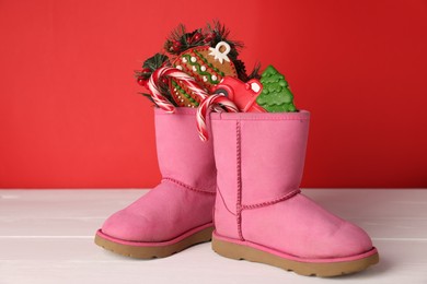 Photo of Saint Nicholas day. Boots with treats and festive decor on white wooden table against red background
