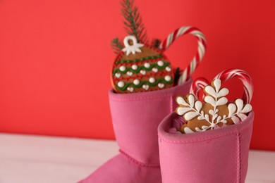 Photo of Saint Nicholas day. Boots with treats and fir branch on white table against red background, closeup. Space for text