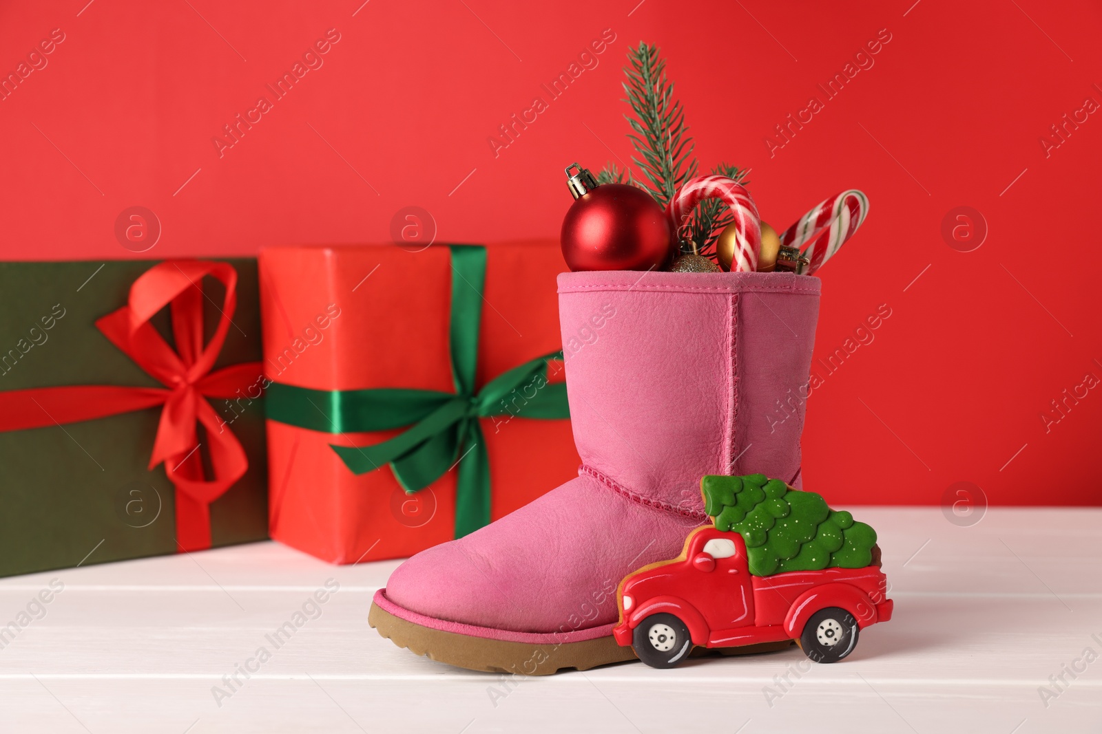 Photo of Saint Nicholas day. Boot with treats, festive decor and gift boxes on white wooden table against red background