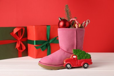 Photo of Saint Nicholas day. Boot with treats, festive decor and gift boxes on white wooden table against red background