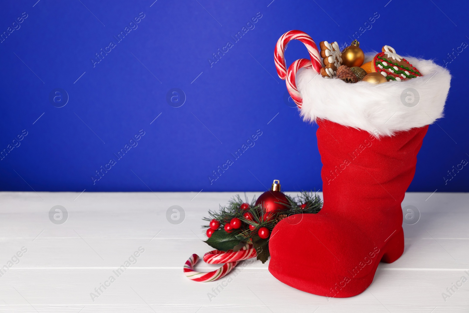 Saint Nicholas day. Red boot with treats and festive decor on white wooden table against blue background. Space for text Photo of Saint Nicholas day. Red boot with treats and festive decor on white wooden table against blue background. Space for text