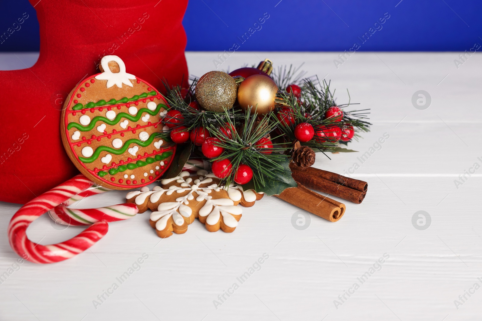 Photo of Saint Nicholas day. Red boot, treats and festive decor on white wooden table, closeup. Space for text