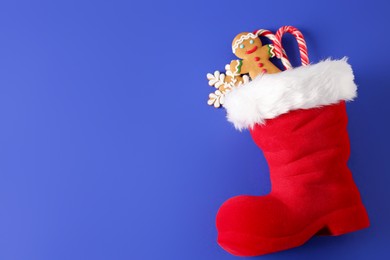 Photo of Saint Nicholas day. Red boot filled with treats on blue background, top view. Space for text