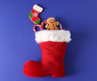 Photo of Saint Nicholas day. Red boot filled with treats on blue background, top view