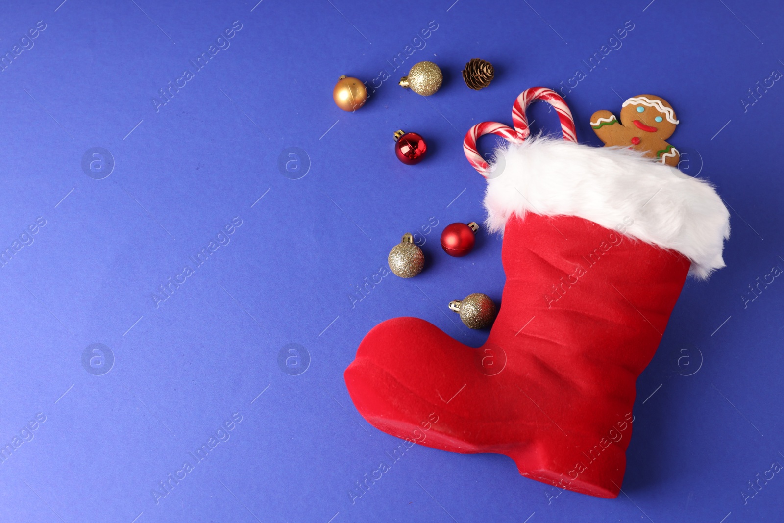 Saint Nicholas day. Red boot filled with treats and ornaments on blue background, flat lay. Space for text Photo of Saint Nicholas day. Red boot filled with treats and ornaments on blue background, flat lay. Space for text
