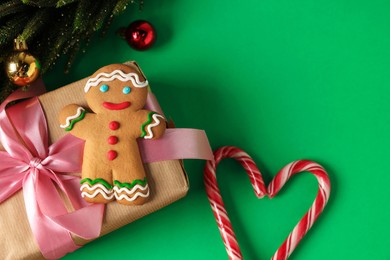 Photo of Saint Nicholas day. Gingerbread man, candy canes, fir tree, ornaments and gift box on green background, flat lay