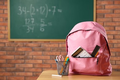 Photo of Pink backpack with different stationery on desk in classroom