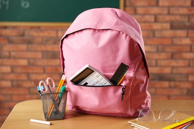 Photo of Pink backpack with different stationery on desk in classroom