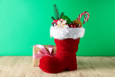 Photo of Happy Saint Nicholas day. Red boot with sweets, festive decor and gift box on wooden table against green background