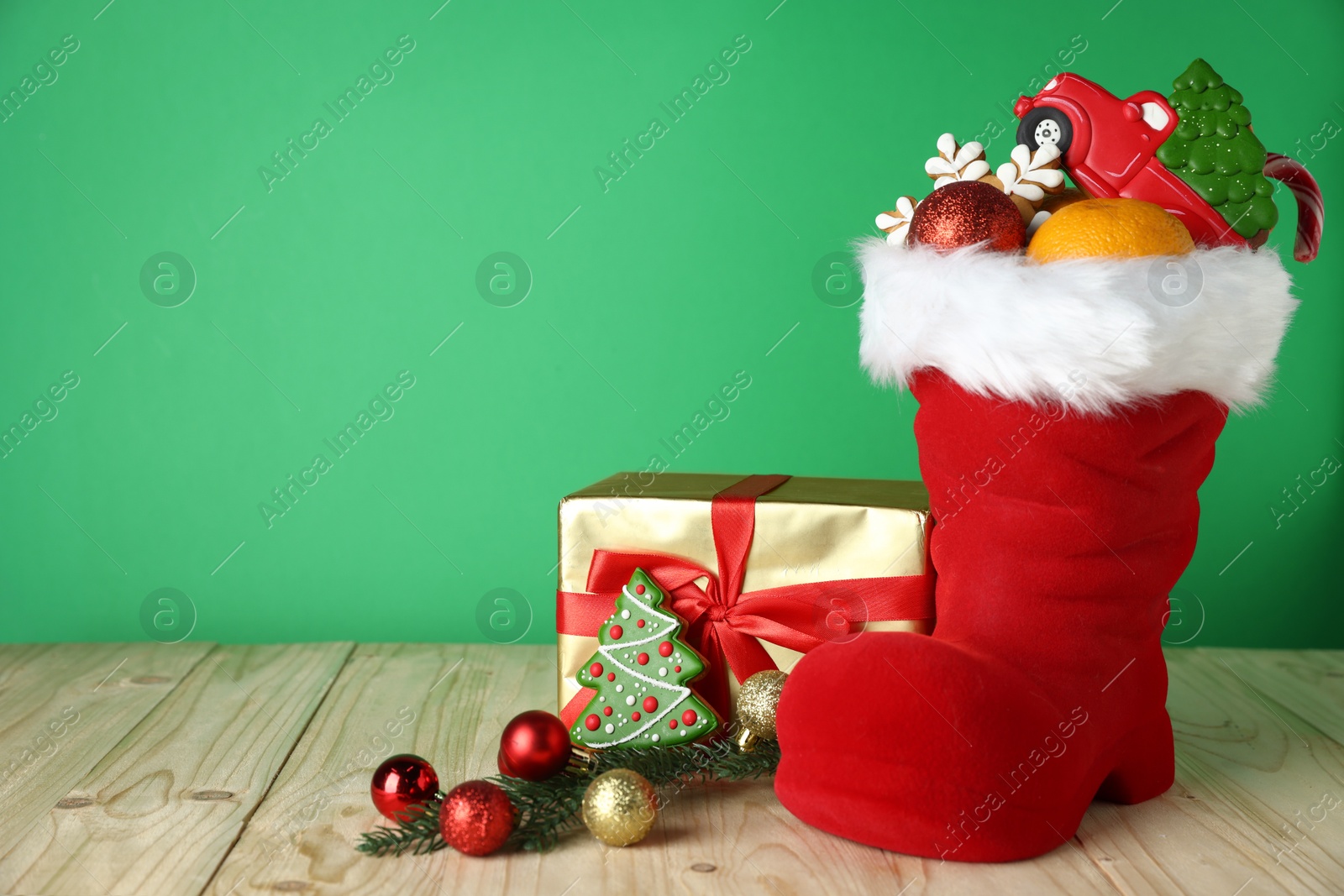 Happy Saint Nicholas day. Red boot with sweets, festive decor and gift box on wooden table against green background. Space for text Photo of Happy Saint Nicholas day. Red boot with sweets, festive decor and gift box on wooden table against green background. Space for text