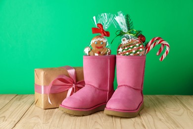 Photo of Happy Saint Nicholas day. Boots with sweets, festive decor and gift box on wooden table against green background