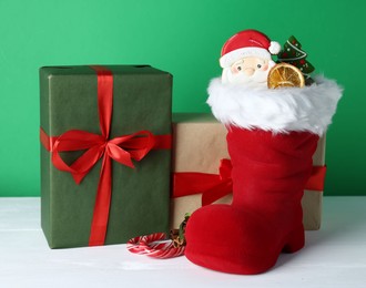 Photo of Happy Saint Nicholas day. Red boot with sweets and gift boxes on white wooden table against green background