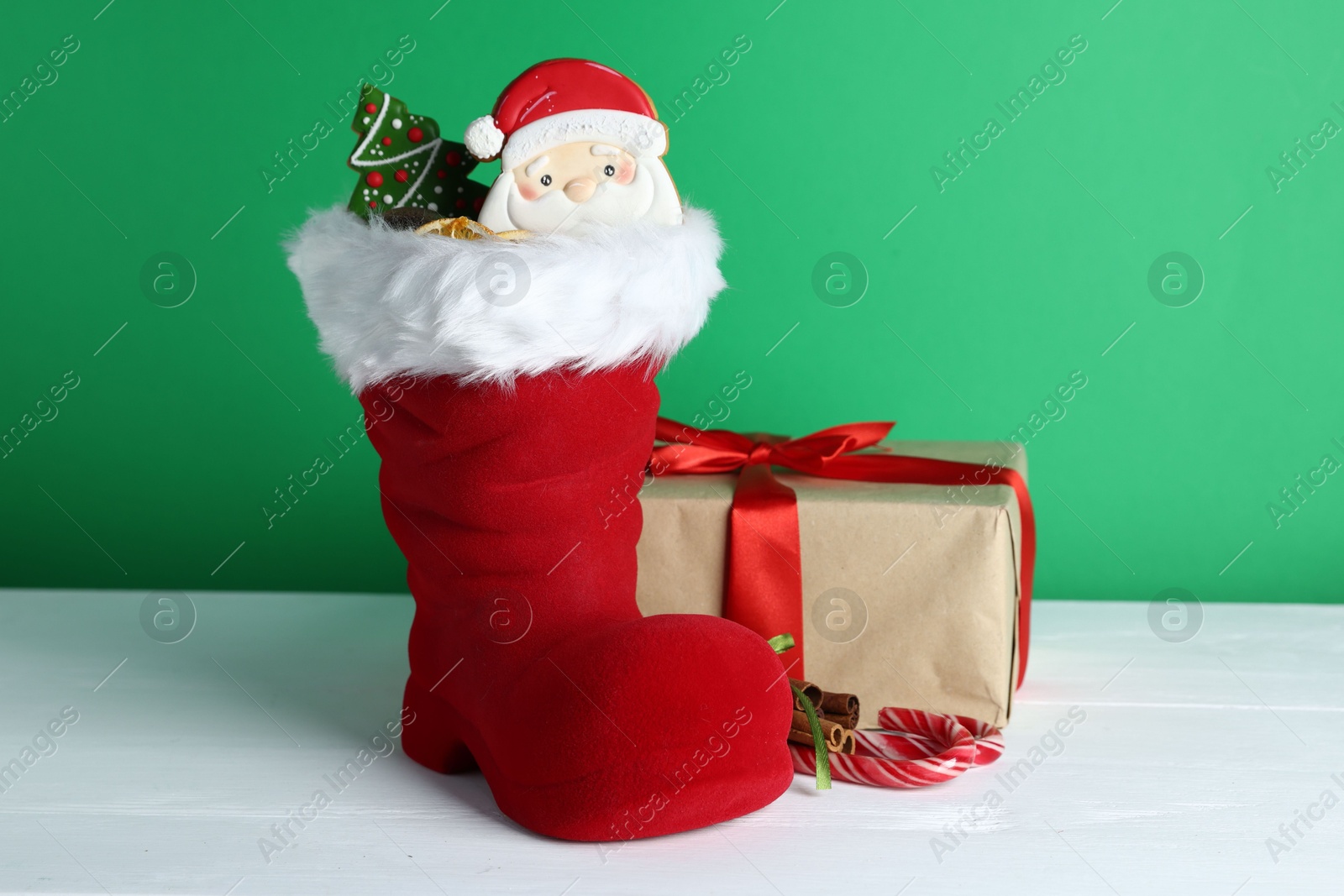 Happy Saint Nicholas day. Red boot with sweets and gift box on white wooden table against green background Photo of Happy Saint Nicholas day. Red boot with sweets and gift box on white wooden table against green background
