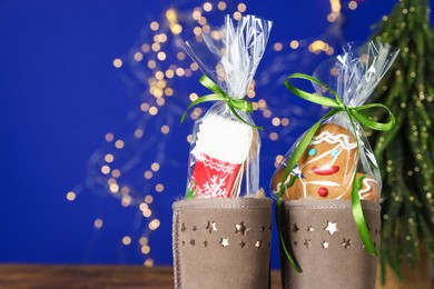 Photo of Happy Saint Nicholas day. Boots with cookies on table against blue background with blurred lights, closeup. Space for text