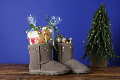 Photo of Happy Saint Nicholas day. Boots with cookies and festive decor on wooden table against blue background