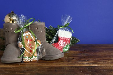 Photo of Happy Saint Nicholas day. Boots with cookies and festive decor on wooden table against blue background, closeup. Space for text