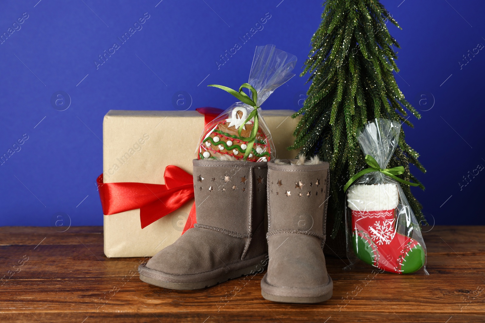Happy Saint Nicholas day. Boots with cookies, artificial fir tree and gift box on wooden table against blue background Photo of Happy Saint Nicholas day. Boots with cookies, artificial fir tree and gift box on wooden table against blue background
