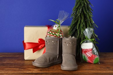 Photo of Happy Saint Nicholas day. Boots with cookies, artificial fir tree and gift box on wooden table against blue background