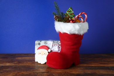 Photo of Happy Saint Nicholas day. Red boot with sweets, festive decor and gift box on wooden table against blue background