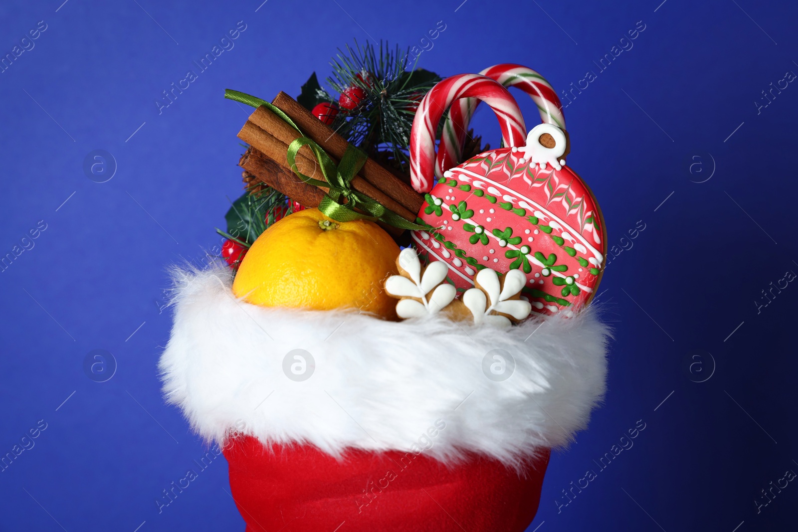 Photo of Happy Saint Nicholas day. Different festive decor, orange and sweets in red boot against blue background, closeup