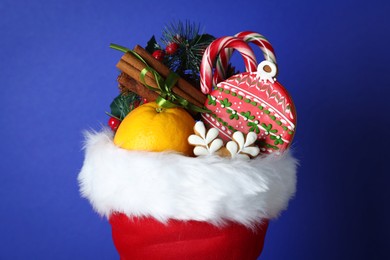 Photo of Happy Saint Nicholas day. Different festive decor, orange and sweets in red boot against blue background, closeup