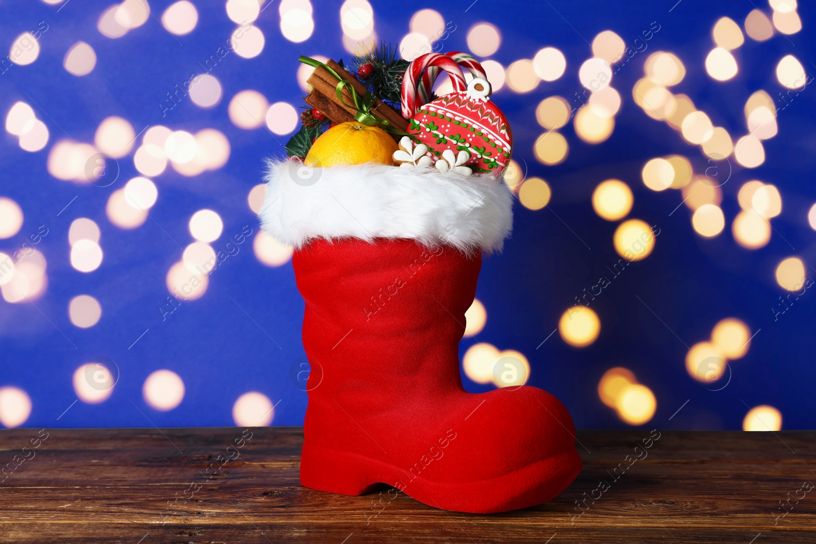 Happy Saint Nicholas day. Red boot with sweets and festive decor on wooden table against blue background with blurred lights Photo of Happy Saint Nicholas day. Red boot with sweets and festive decor on wooden table against blue background with blurred lights