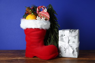Photo of Happy Saint Nicholas day. Red boot with sweets, festive decor and gift box on wooden table against blue background
