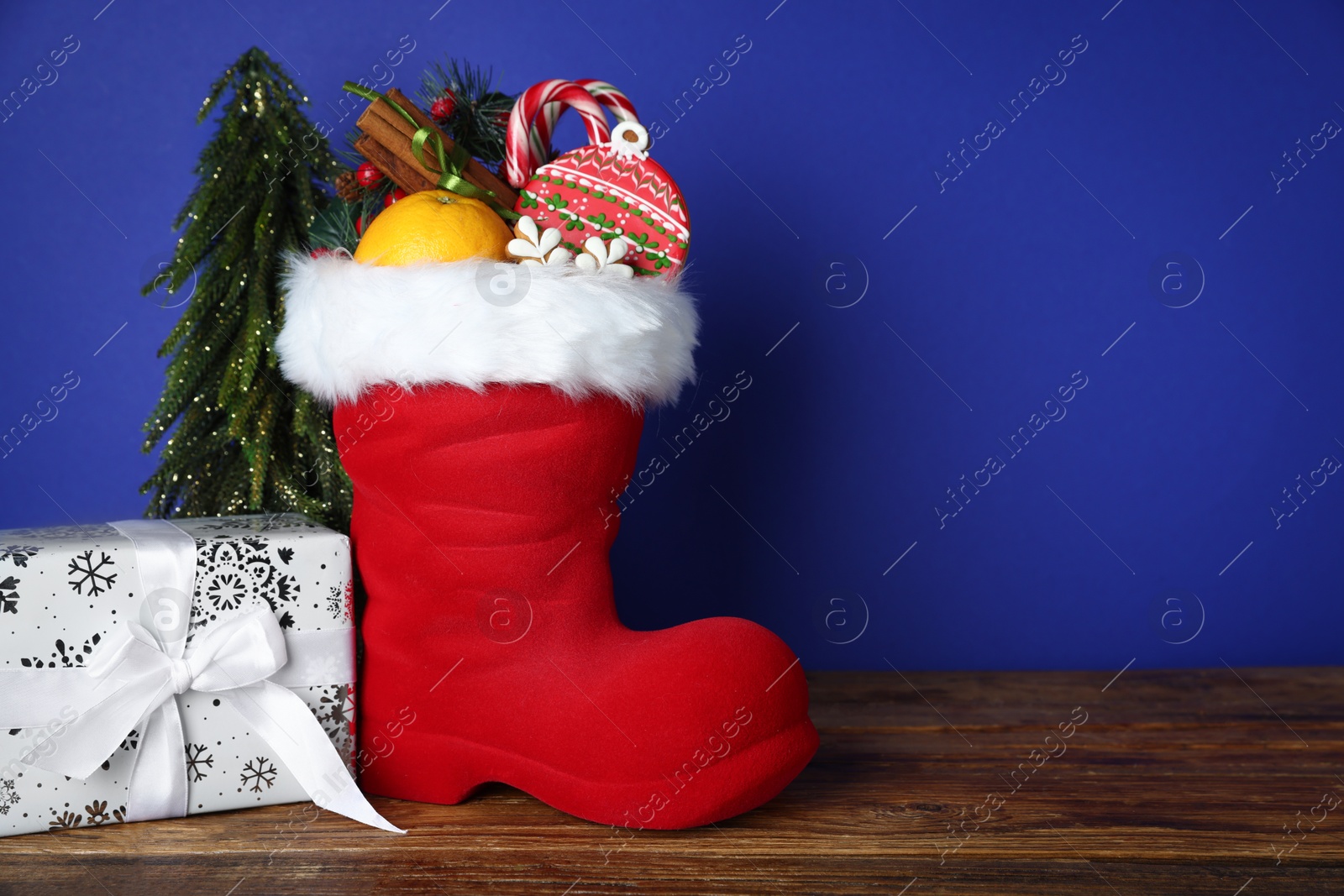 Happy Saint Nicholas day. Red boot with sweets, festive decor and gift box on wooden table against blue background. Space for text Photo of Happy Saint Nicholas day. Red boot with sweets, festive decor and gift box on wooden table against blue background. Space for text