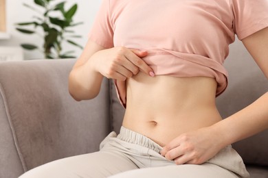Photo of Woman with flat belly on sofa at home, closeup