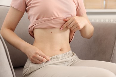 Photo of Woman with flat belly on sofa at home, closeup