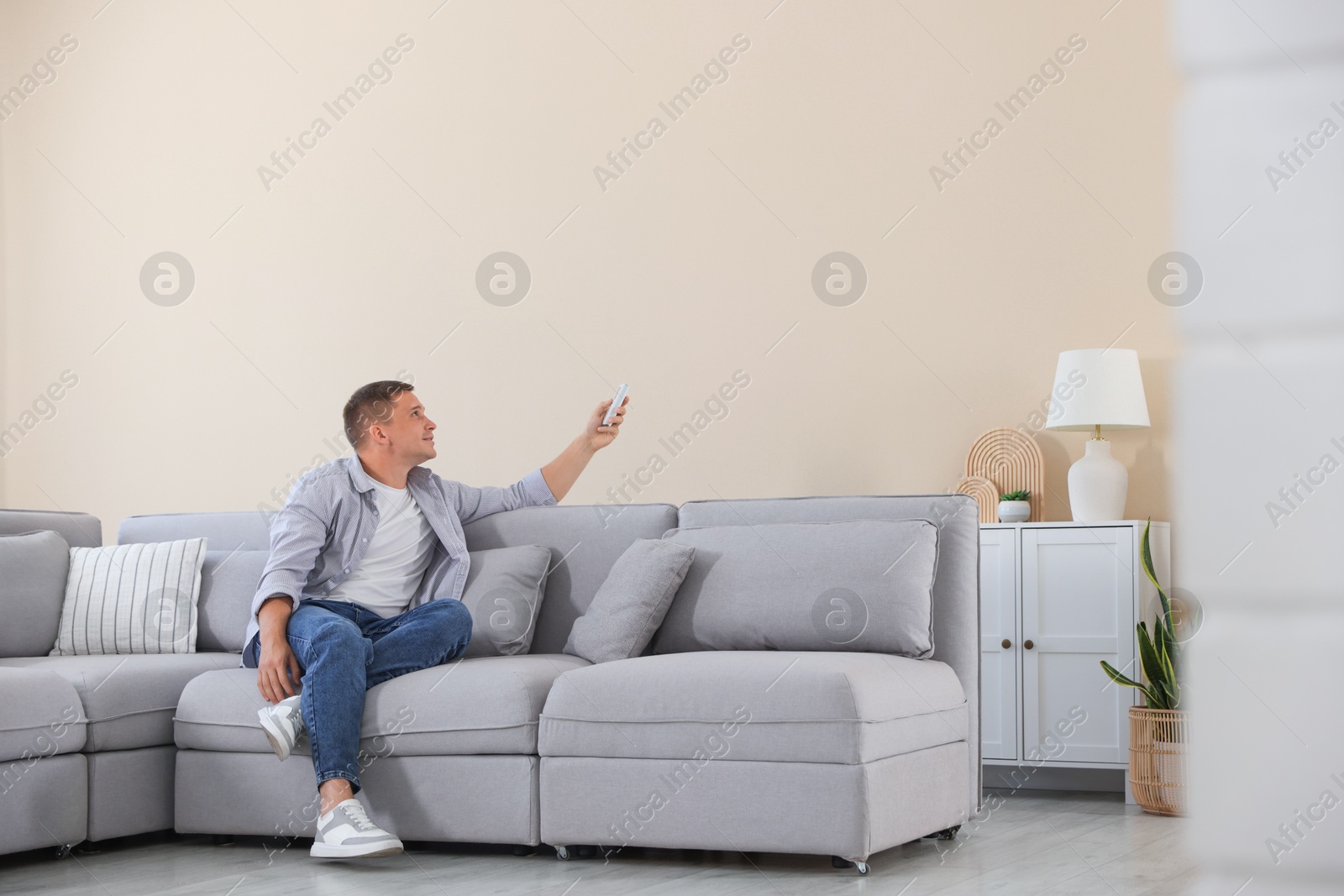 Man using remote to control air conditioner on sofa at home Photo of Man using remote to control air conditioner on sofa at home