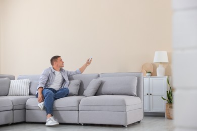 Photo of Man using remote to control air conditioner on sofa at home