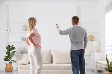 Photo of Woman and man using remote to control air conditioner at home, back view
