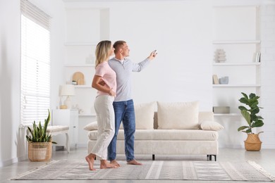 Photo of Woman and man using remote to control air conditioner at home