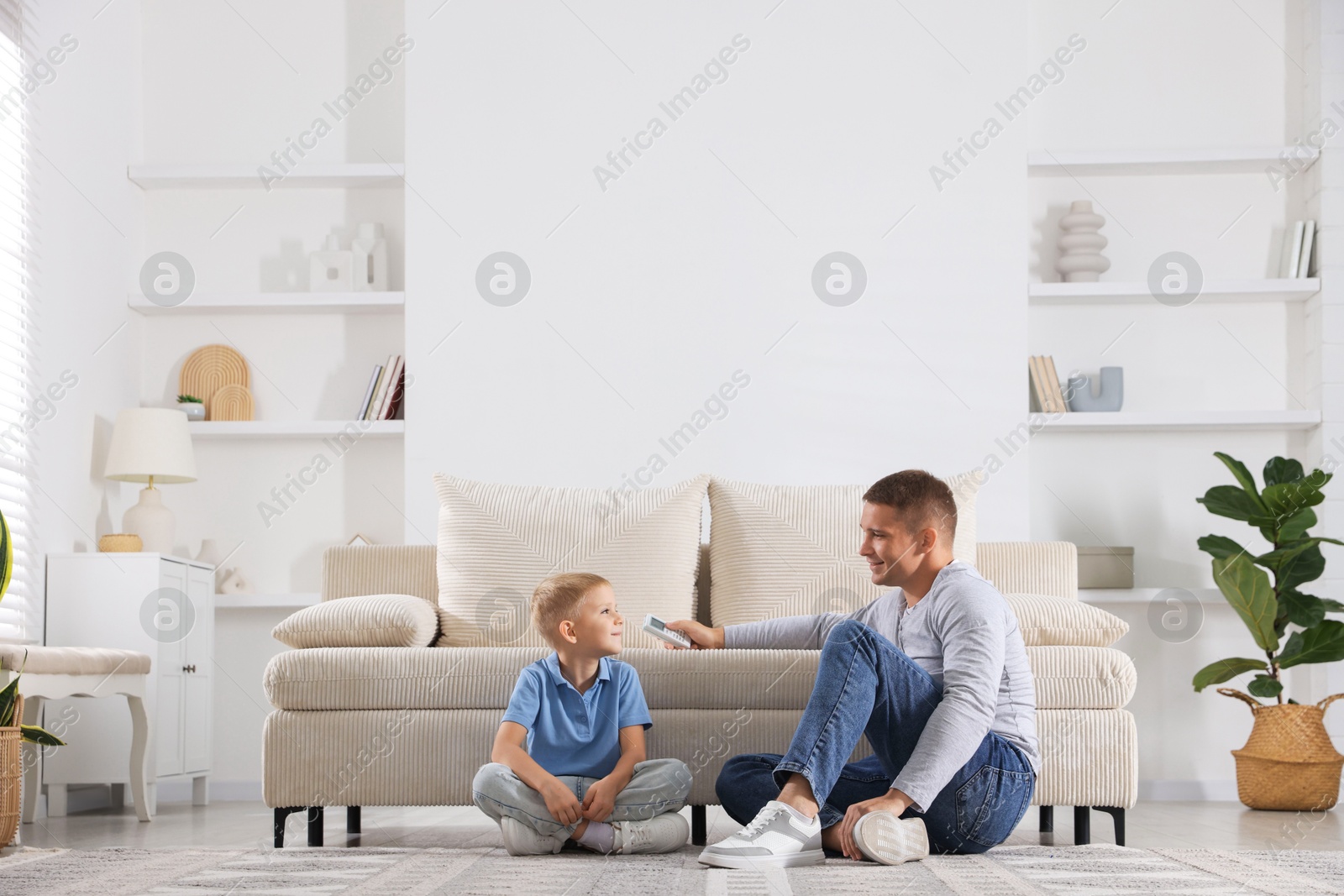 Photo of Cute little boy and his father using remote to control air conditioner at home