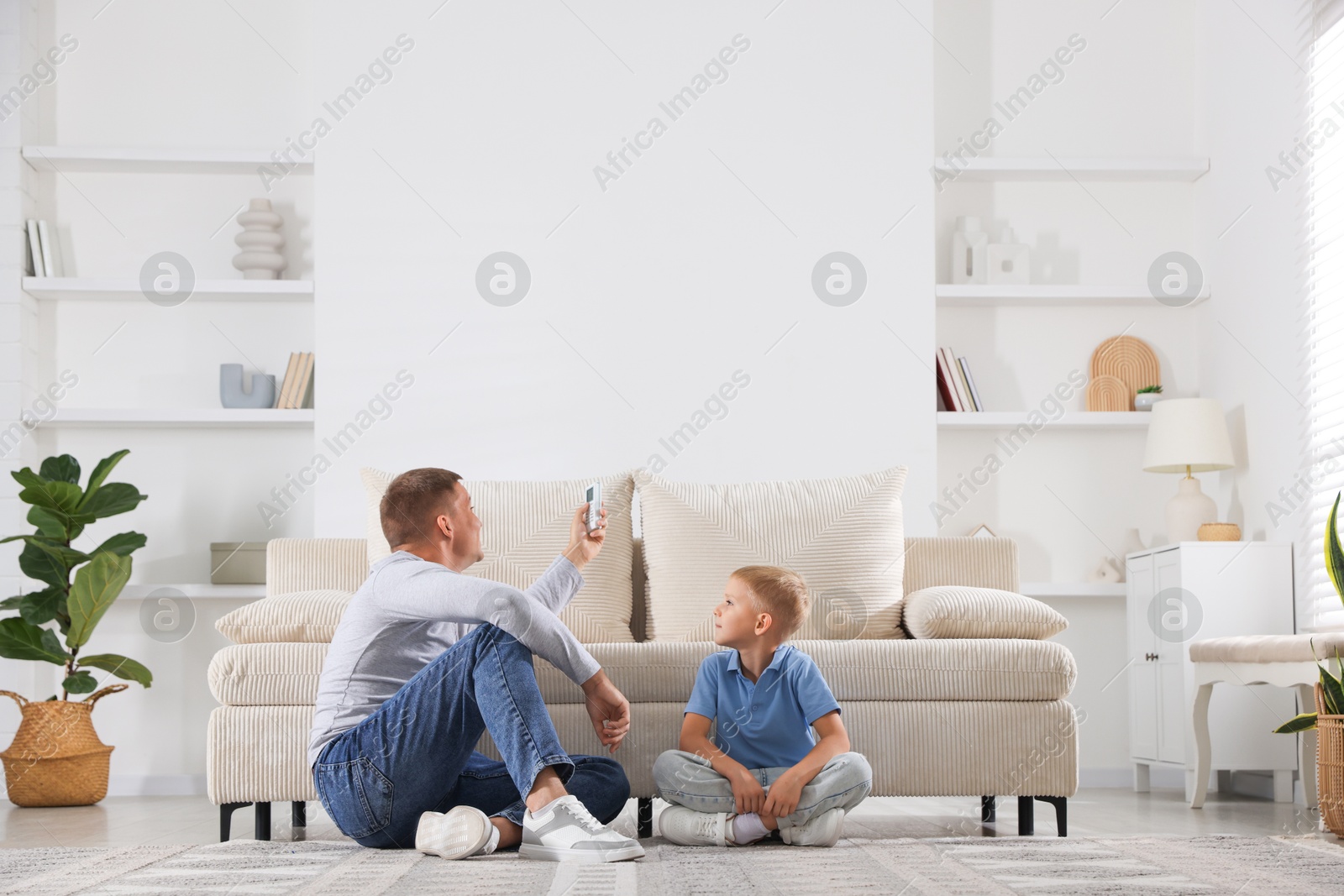 Photo of Cute little boy and his father using remote to control air conditioner at home