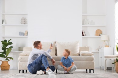 Photo of Cute little boy and his father using remote to control air conditioner at home