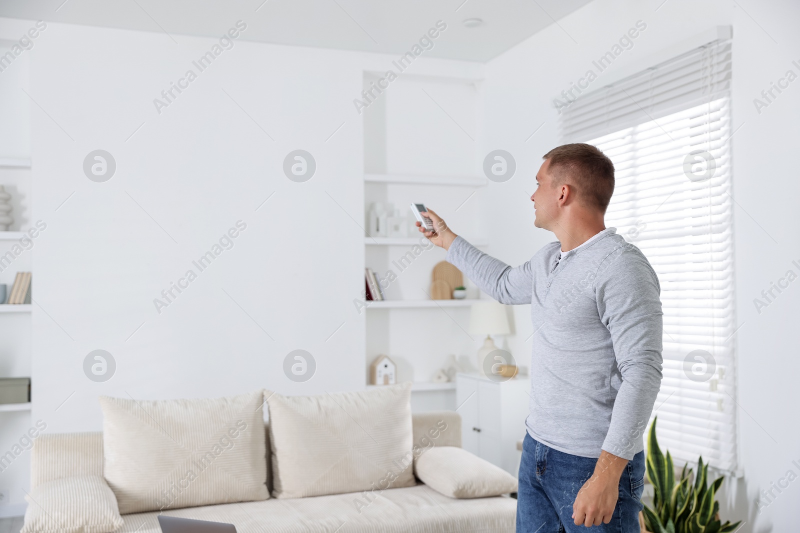 Man using remote to control air conditioner at home. Space for text Photo of Man using remote to control air conditioner at home. Space for text