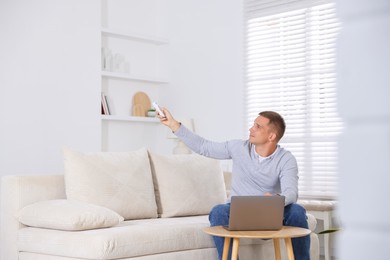 Photo of Man using remote to control air conditioner on sofa at home