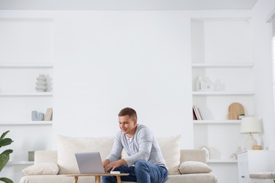 Photo of Young man using laptop on sofa at home