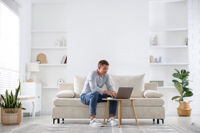 Photo of Young man using laptop on sofa at home