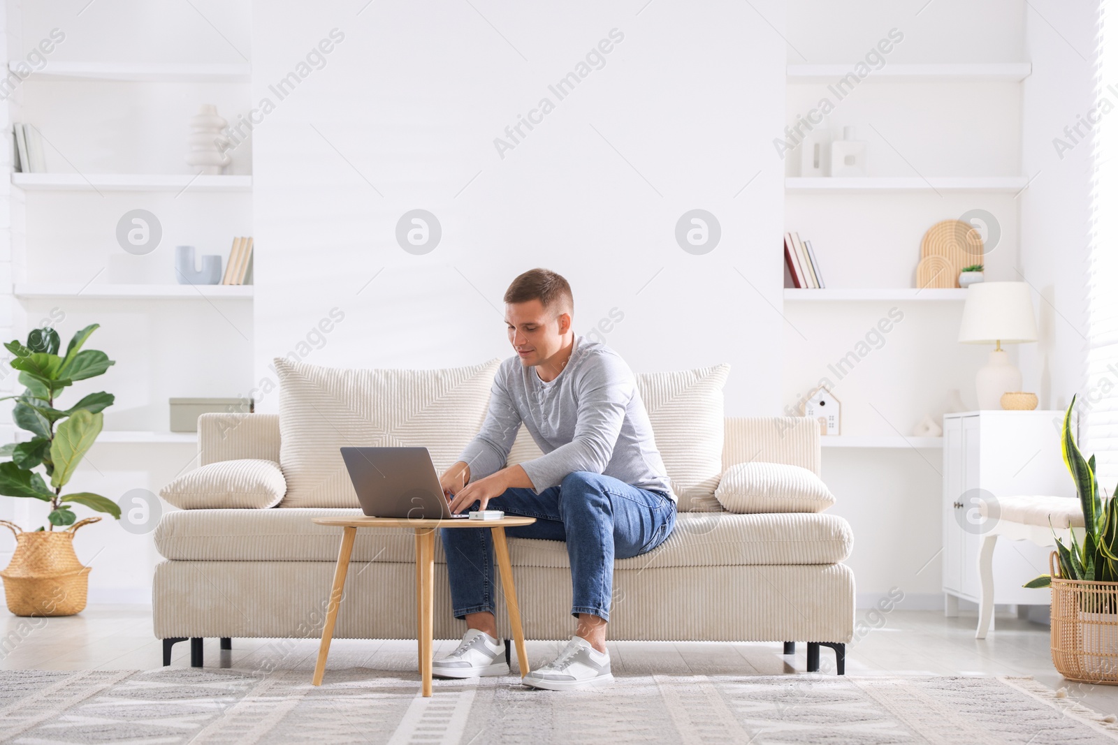 Photo of Young man using laptop on sofa at home